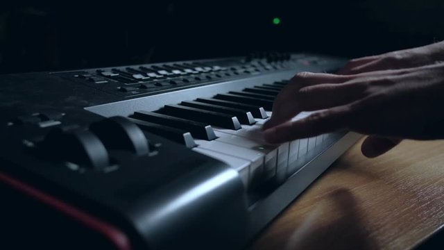 Musician playing on musical keyboard. Close up of a hand playing a MIDI controller keyboard in black background.
