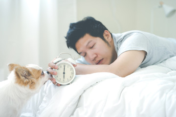 Sleepy young asian man wake up early in morning with eyes still close holding alarm watch in hand...
