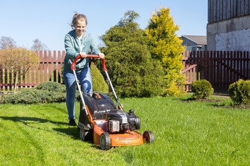 Fototapeta premium teenage girl working in garden, mowing grass with lawn-mower