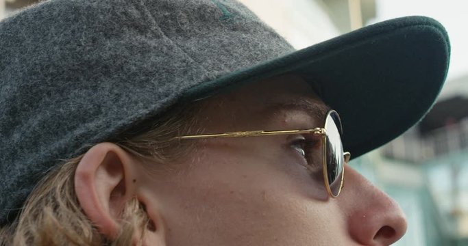 Close-up of a hipster in sunglasses and a cap who looks out onto the street in slow motion