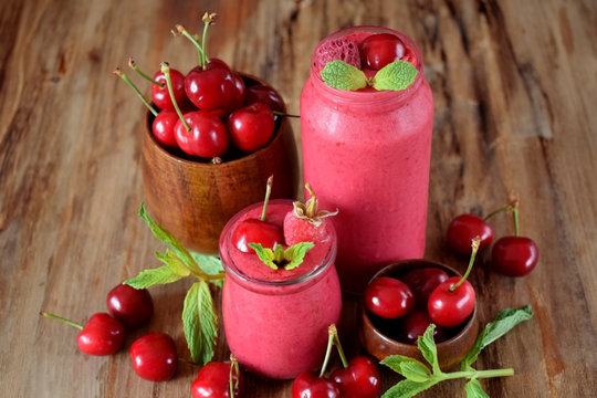 Red smoothie made of cherries in glass jars. Berries are around on a wooden table