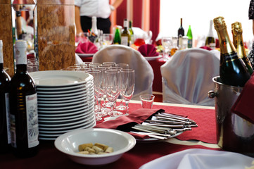 Table appointments for guests. Red tablecloth, white plates, cutlery, wineglasses and bottles of wine on the table.