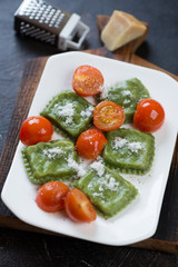 Spinach ravioli with cherry tomatoes and grated parmesan served on a white plate, vertical shot