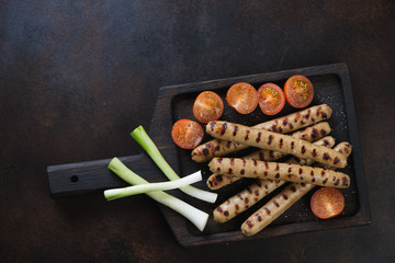 Black wooden serving tray with grilled italian style sausages, flatlay on a dark brown metal background, horizontal shot