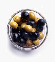 Green and black olives in bowl on white surface isolated.