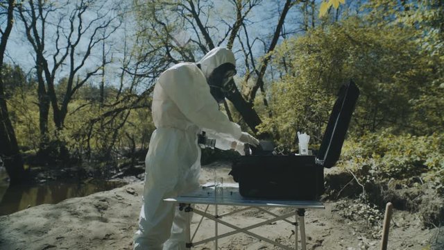 The scientist in a chemical protective suit takes pictures of a large spider on infected territory and makes notes in a notebook. Biohazard zone.