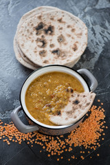 Pan with thick red lentil indian soup masoor dal and chapati, elevated view, grey concrete background