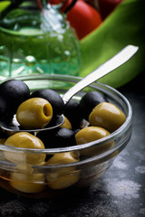 Green and black olives in bowl on black surface in front of oil bottle. Close up.