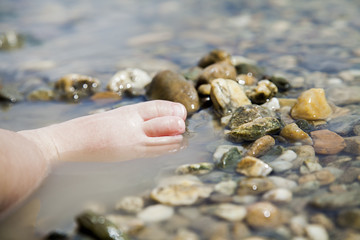 Child playing with her feet and rocks in lake