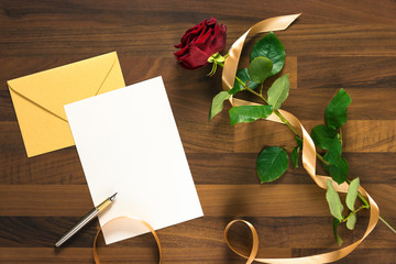 blank white paper with pen on yellow envelope and red rose on the wooden table