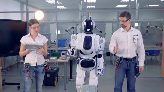 Male engineer and a cyborg are moving synchronically under supervision of a female engineer