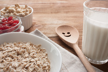 Oatmeal with dried cherries, cashews, milk and a wooden spoon on wooden table.