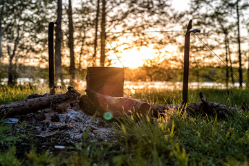 Tourist boiling pot at the stake in the forest at sunset