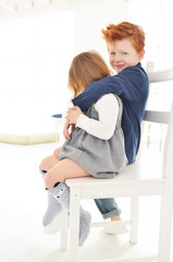 Cute kids red boy brother and blonde sister have a fun on the swing in the white studio