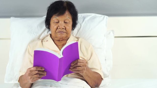 old woman reading a book on bed in bedroom