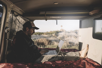 Adventurous man working with computer inside a van.