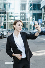 A young woman in a business suit crosses the street. Business woman talking through a mobile phone. A girl with a notepad and a phone near the office.