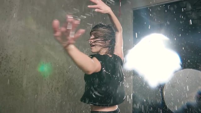 Modern dance wet young woman in the rain on stage. Wet dancer girl dancer circling around herself in the studio under the rain water