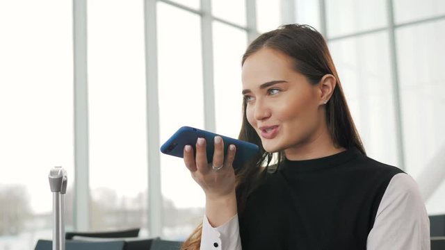 Portrait of a girl using the voice recognition of the phone and looking at cell phone near airport terminal in hotel on vacation tourist speech personal assistant natural language user interface