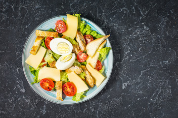 Fototapeta na wymiar Fresh caesar salad in plate on black stone table. Top