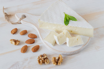 Fresh Brie cheese and a slice on a wooden board with nuts