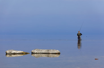Angler walking in the blue calm sea trying to catch trout at Aleklinta on the island Oland, Sweden