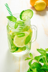 Detox water infused with sliced lemon, cucumber and sprigs of mint on wooden background.