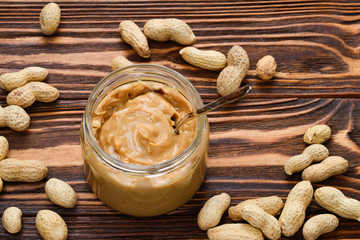 Bowl of peanut butter and peanuts on dark wooden background from top view. Space for text or design.