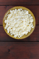 Cottage cheese on wooden boards, soft cheese on a yellow plate. Dairy product on a brown wooden background, healthy lifestyle. Copy space