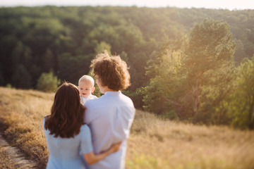 Young happy caucasian couple with baby boy. Parents and son having fun together. Mother and father play with toddler outdoors. Family, parenthood, childhood. Tilt-shift image, soft selective focus.