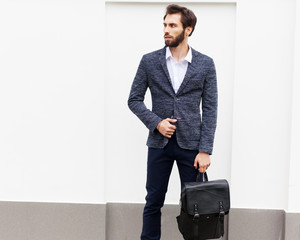 Young businessman with a beard in a fashionable suit and a trendy backpack posing against a white...