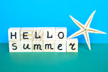 Wooden cubes with written words Hello summer and starfish on the blue background.