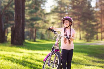 Happy child in a protective helmet before riding a bike in the Park. Active leisure for children. girl holding a bicycle and laughing