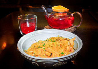 Чай из лесных ягод фруктовый с долькой апельсина на деревянной подставке со стаканом и тарелка со стеклянной лапшой и морепродуктами