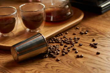 Fototapeta na wymiar Coffee beans, metal cup and glass cup of coffee drink on wooden table background, close-up.
