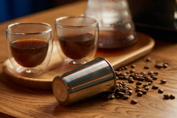 Fototapeta na wymiar Coffee beans, metal cup and glass cup of coffee drink on wooden table background, close-up.