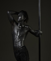 Man with nude torso covered with shimmering paint, dark background.