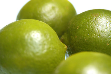 Four whole limes on a white background. Whole limes, shallow depth of field, focus on one lime. Group of limes on a white table in the studio, close up shot.