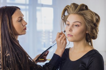 Makeup artist applying liquid tonal foundation on the face of the woman in white make up room. Beauty and fashion concept
