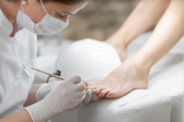 Professional in beauty salon cleaning nails on feet.