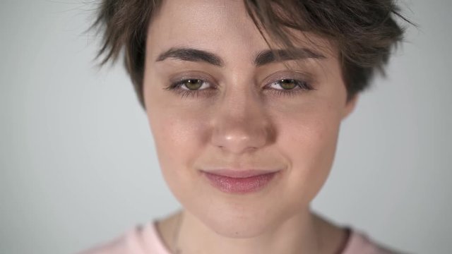 Portrait of a young woman with short brown hair, big eyes and full lips blinking and half smiling to someone off camera. Locked down real time medium shot