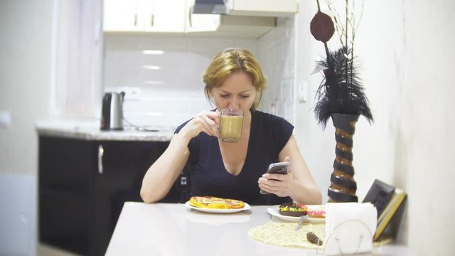 woman is eating pizza in the kitchen at home and using her smartphone, 4k, background blur