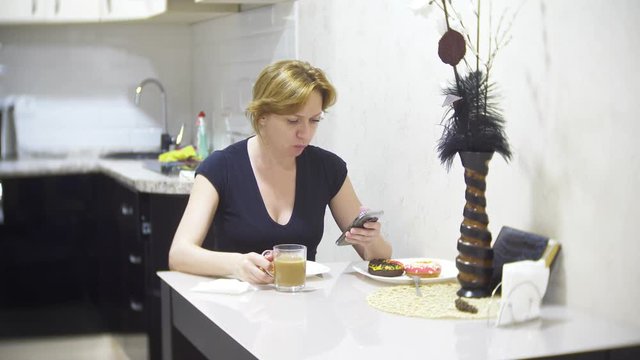 woman is eating pizza in the kitchen at home and using her smartphone, 4k, background blur