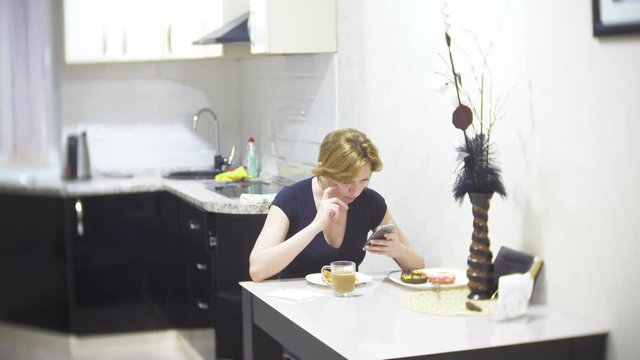 woman is eating pizza in the kitchen at home and using her smartphone, 4k, background blur