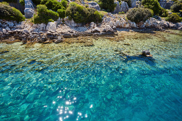 Sunken city of Kekova in bay of Uchagiz view from sea in Turkey with turqouise sea rocks and green bushes with remains of ancient city visible under water.