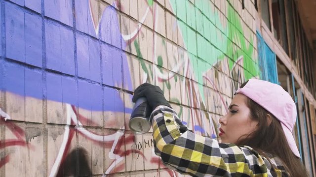 Young woman graffiti artist drawing on the wall, close up, slow motion