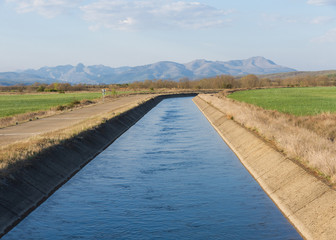 Canal de agua para el riego en paisaje con montañas al fondo