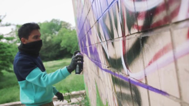 Young man graffiti artist painting on the wall, slow motion, dolly shot