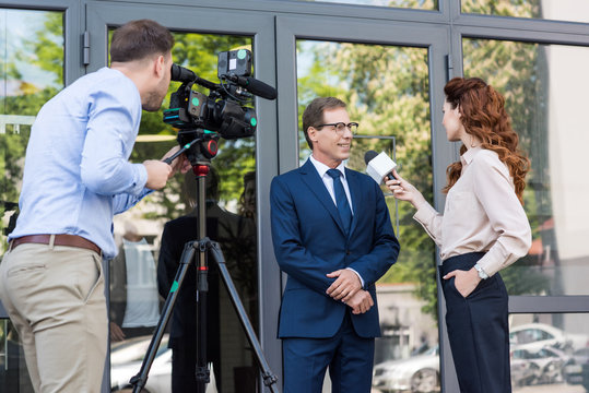 cameraman and news anchor interviewing businessman near office building