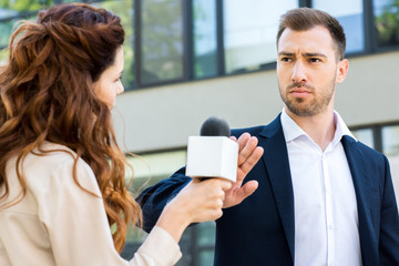 anchorwoman holding microphone while serious businessman refusing interview